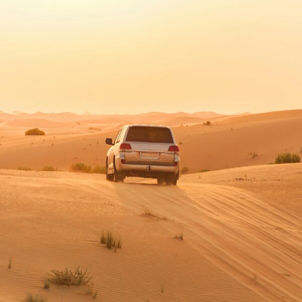 A white SUV driving through the sand dunes of the Arabian desert at sunset, capturing adventure and solitude.